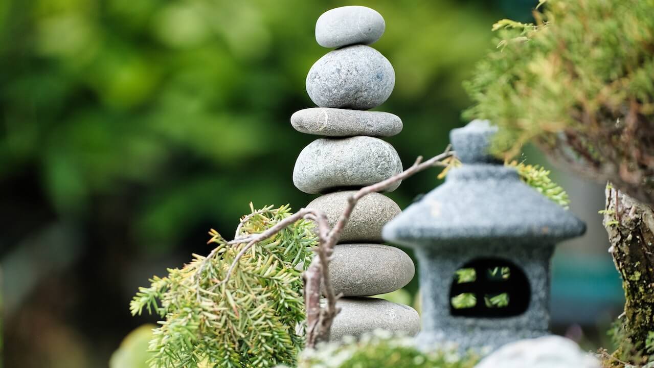 A close-up of a miniature house and stacked rocks near it that represents house-leveling shims.